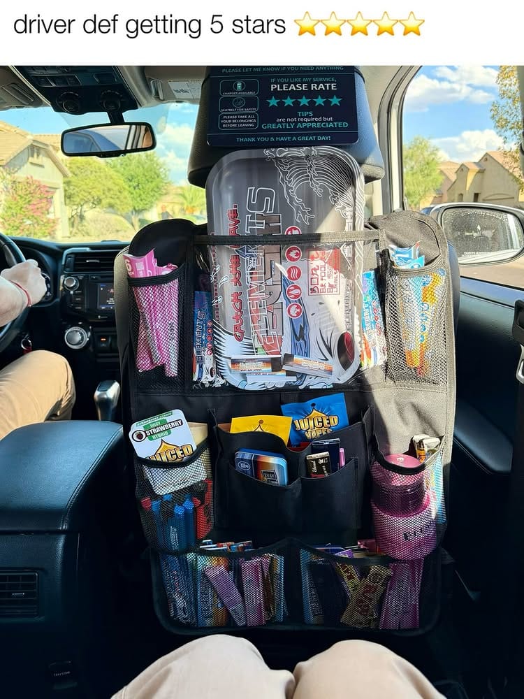 A view from the back seat of a car showing a black seatback organizer packed with smoking and vaping supplies, including a large Elements rolling tray, various packs of Elements rolling papers, and Juiced Vapes. A rideshare tip and rating sign hangs on the headrest above it, and a text overlay at the top reads 'driver def getting 5 stars' with five star emojis.