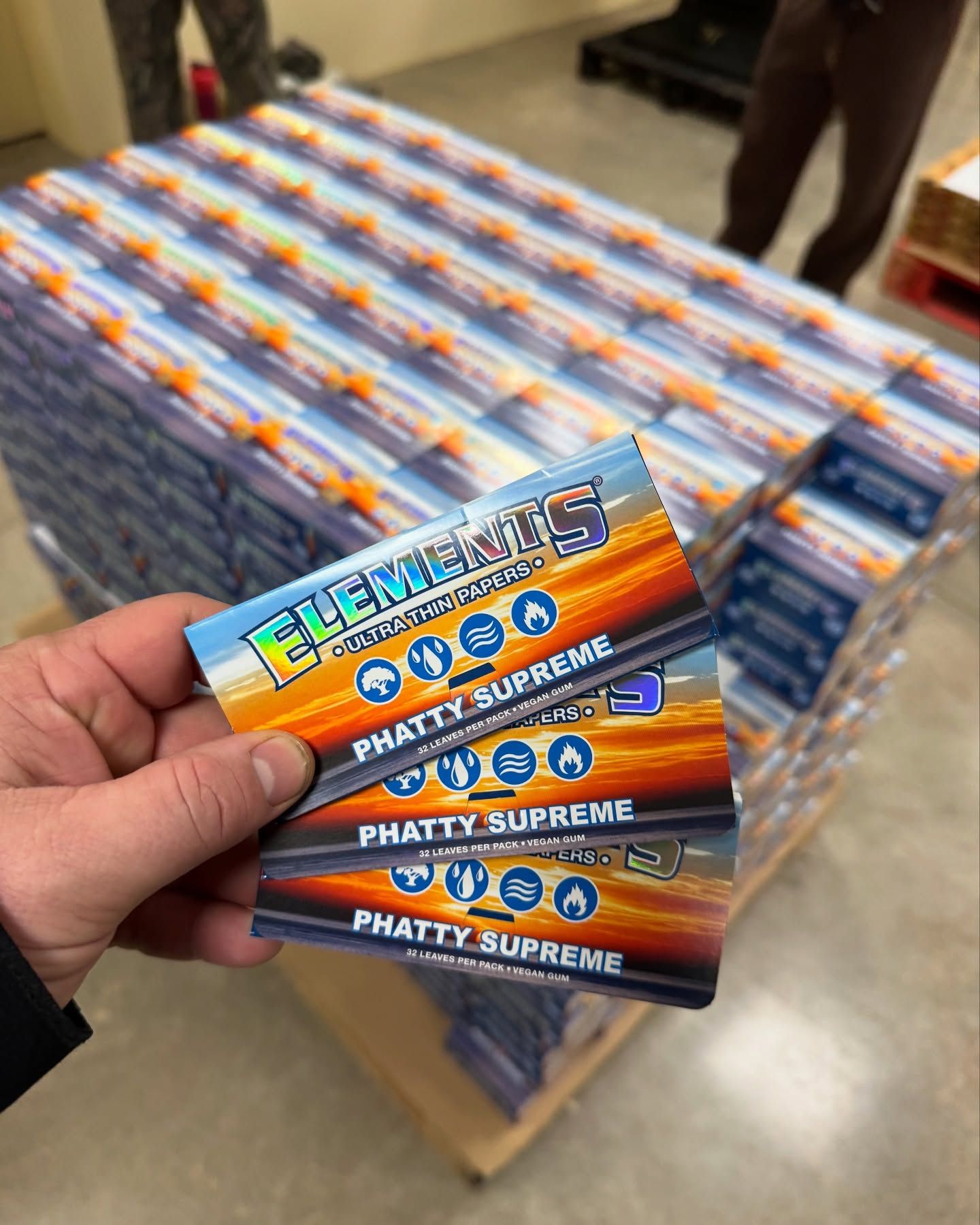A hand holding three packs of Elements Phatty Supreme rolling papers.